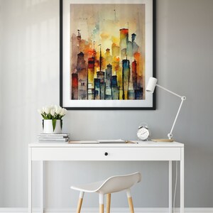 May include: A white desk with a drawer and a black frame picture of a watercolor painting of a city skyline. The desk has a white lamp and a white chair with wooden legs. The painting is on a light gray wall.