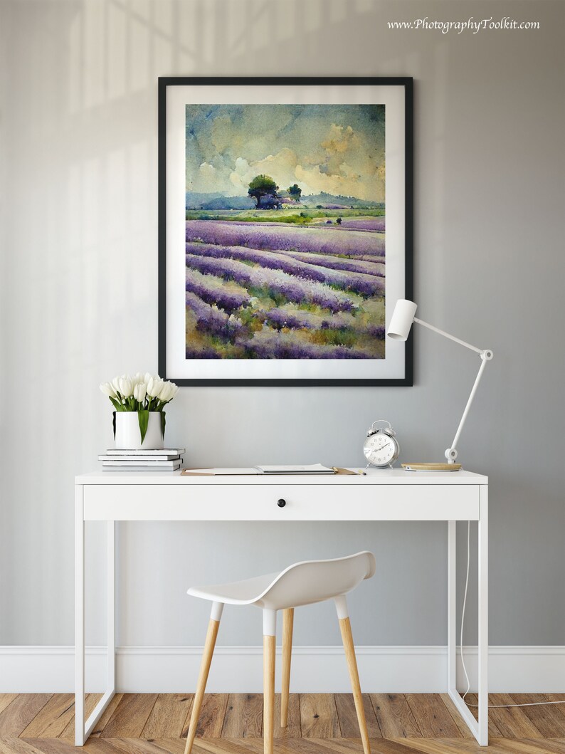 May include: A framed watercolor painting of a lavender field with a small house and trees in the distance. The painting is hanging on a gray wall above a white desk with a white chair and a white lamp.