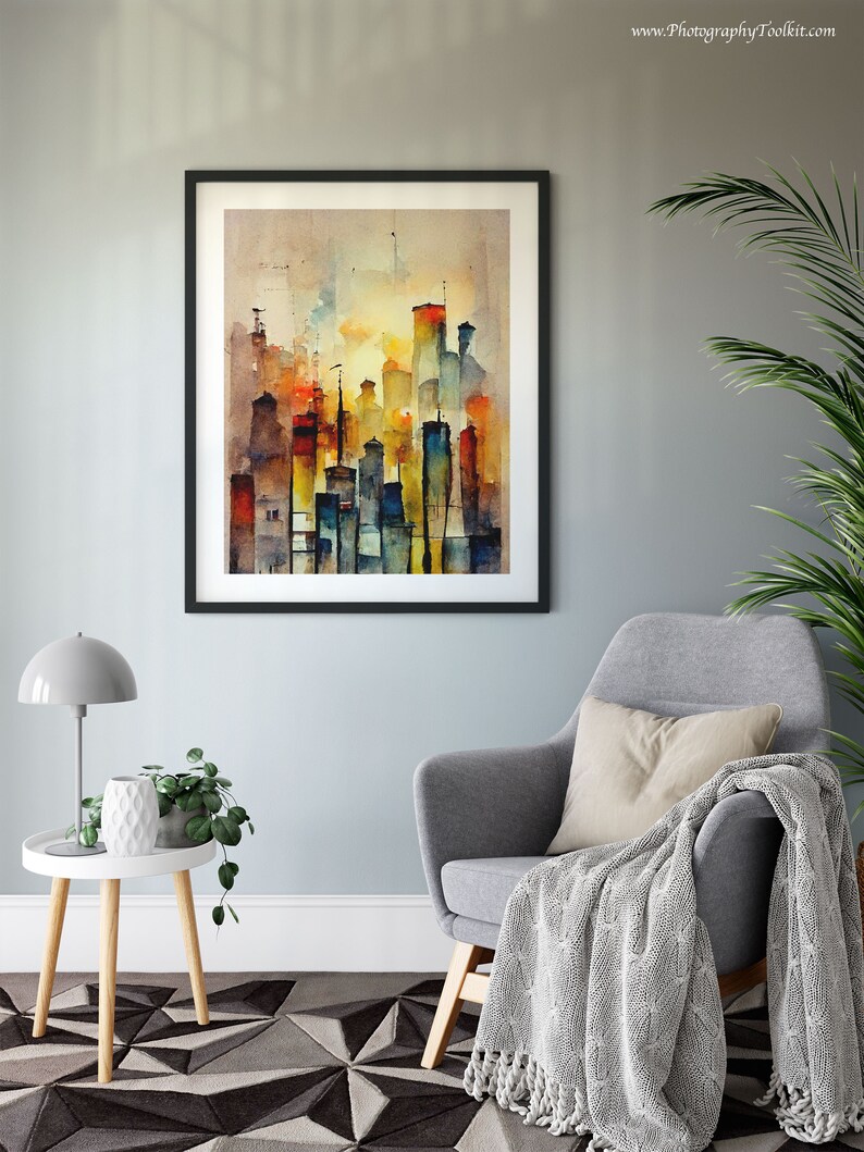 May include: A framed watercolor painting of a city skyline in shades of blue, yellow, orange, and red. The painting is hanging on a light gray wall above a gray armchair with a white throw blanket.