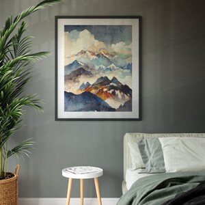 May include: A framed watercolor painting of a mountain range with clouds and a blue sky. The painting is in a black frame and is hanging on a gray wall. There is a white side table with a magazine on it and a green bed with white pillows in the foreground.