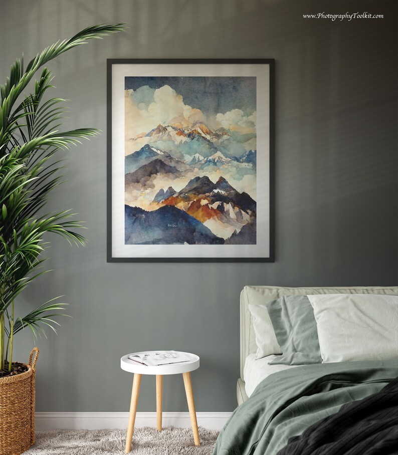 May include: A framed watercolor painting of a mountain range with clouds and a blue sky. The painting is in a black frame and is hanging on a gray wall. There is a white side table with a magazine on it and a green bed with white pillows in the foreground.