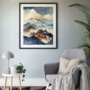 May include: A framed watercolor painting of a mountain range with blue, brown, and white peaks. The mountains are surrounded by clouds and fog. The painting is in a black frame and is hanging on a light gray wall.
