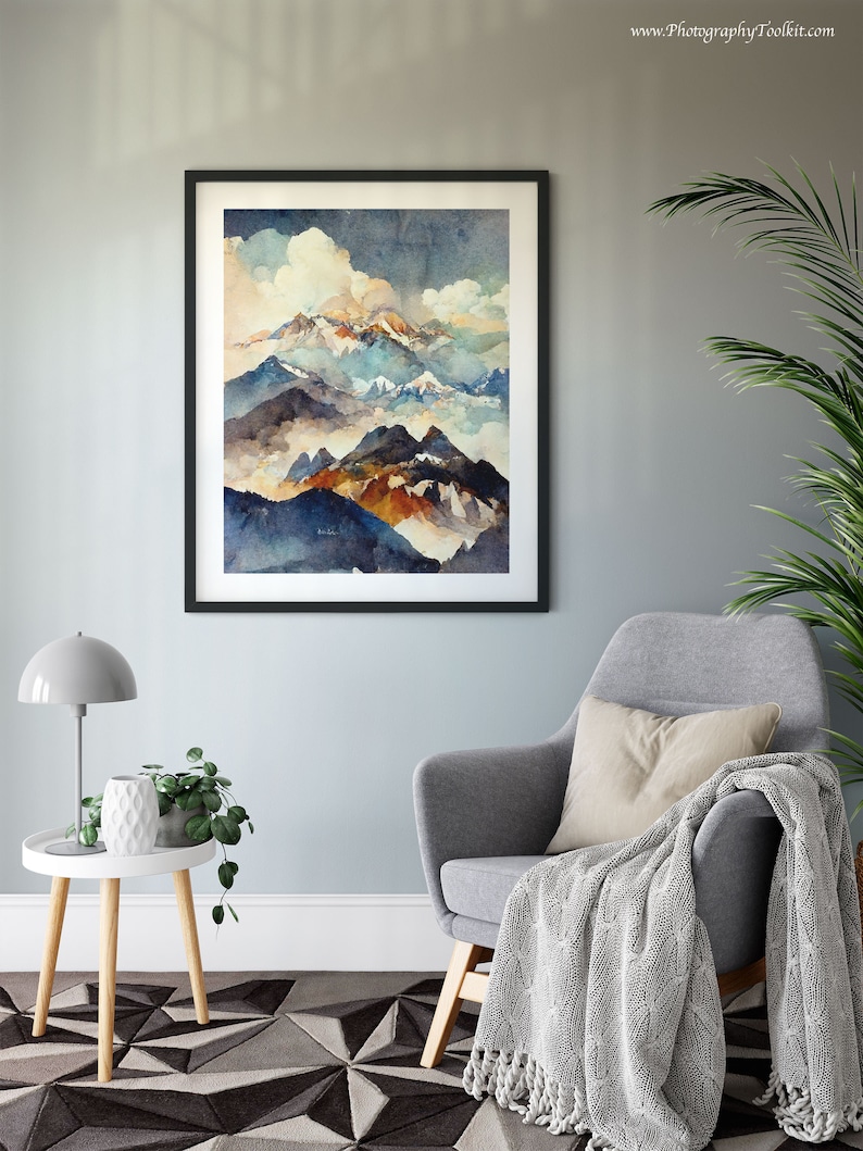 May include: A framed watercolor painting of a mountain range with blue, brown, and white peaks. The mountains are surrounded by clouds and fog. The painting is in a black frame and is hanging on a light gray wall.