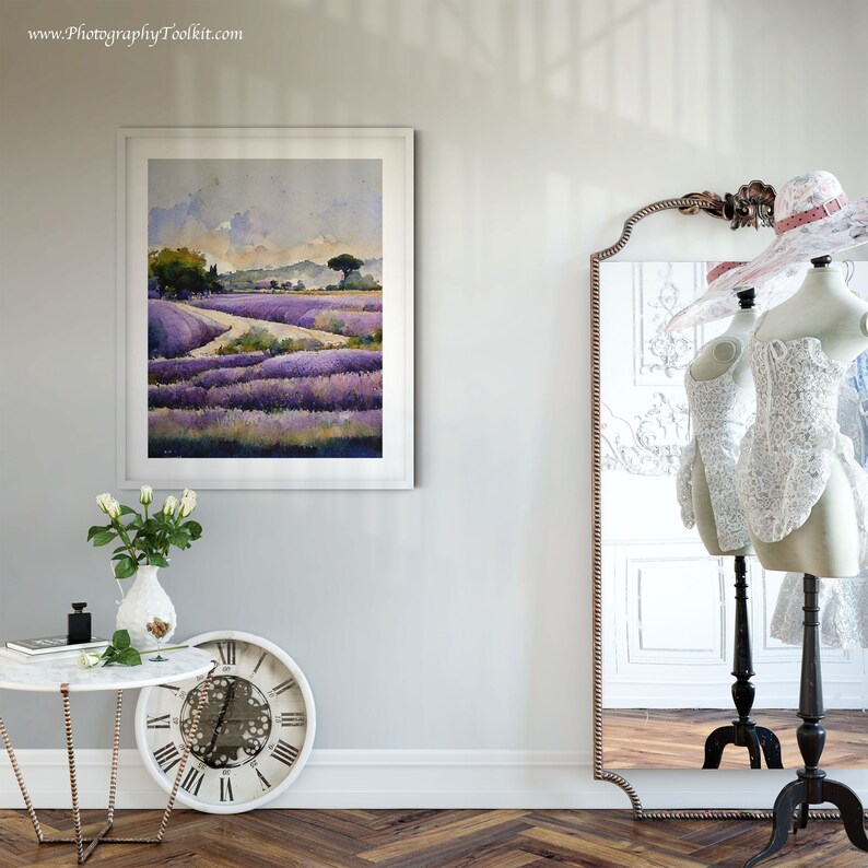 May include: A framed watercolor painting of a lavender field with a winding path leading to a small village in the distance. The painting is hanging on a white wall next to a mirror and a table with a vase of white roses.