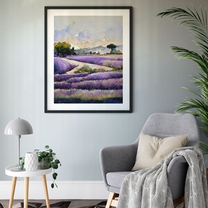 May include: A framed watercolor painting of a lavender field with a winding path leading to a small tree in the distance. The painting is hanging on a light gray wall above a gray armchair with a white throw blanket.