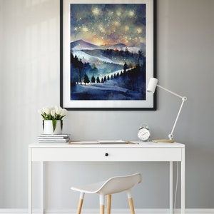 Pode incluir: Uma pintura a aquarela emoldurada de uma paisagem montanhosa nevada com um c&eacute;u estrelado noturno. A pintura est&aacute; pendurada em uma parede cinza acima de uma mesa branca com uma cadeira branca.