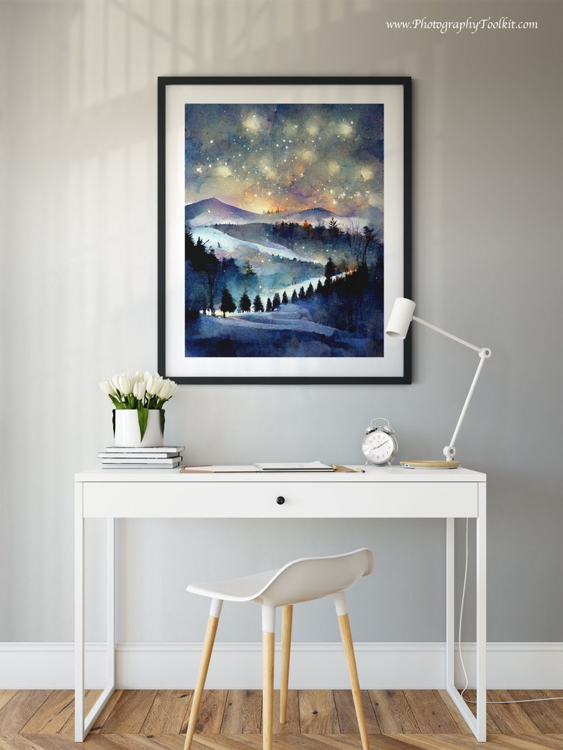 Pode incluir: Uma pintura a aquarela emoldurada de uma paisagem montanhosa nevada com um c&eacute;u estrelado noturno. A pintura est&aacute; pendurada em uma parede cinza acima de uma mesa branca com uma cadeira branca.