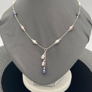 May include: A silver chain necklace with a drop pendant featuring a cluster of pearls in white, pink, and black. The necklace is adorned with a series of pearls in the same colors.