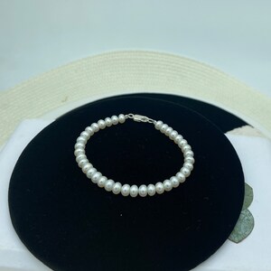 May include: A white pearl bracelet with a silver clasp. The bracelet is on a black background.
