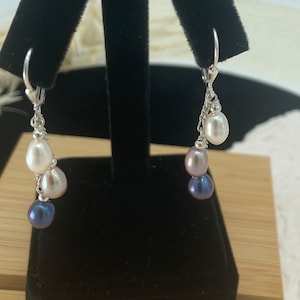 May include: A pair of silver dangle earrings with three pearls each. The top pearl is white, the middle pearl is pink, and the bottom pearl is dark blue.