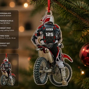 May include: A clear acrylic Christmas ornament featuring a motocross rider on a dirt bike. The rider wears a red and white helmet, black and white gear, and a black chest protector with the name KAYDEN and the number 125 printed in white.