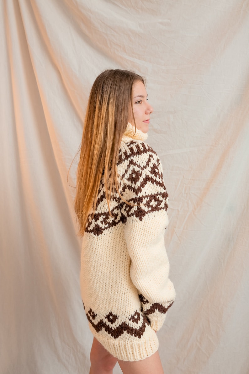May include: A white knitted sweater with a brown geometric pattern. The sweater has a turtleneck and long sleeves.