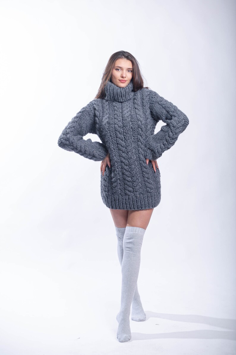 May include: A gray cable knit sweater dress with a turtleneck. The sweater is worn with gray knee-high socks.