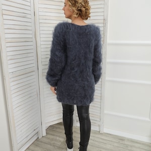 May include: A long-sleeved, fuzzy, dark blue sweater with a v-neck. The sweater is worn by a person with curly blonde hair. The person is wearing black leggings and black shoes.