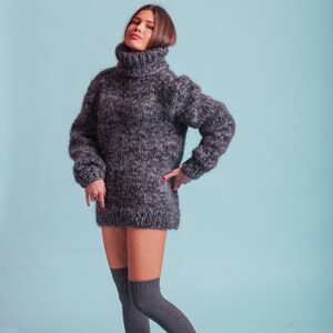 May include: A woman wearing a gray turtleneck sweater and gray knee-high socks. The sweater is a loose fit and has a fuzzy texture.