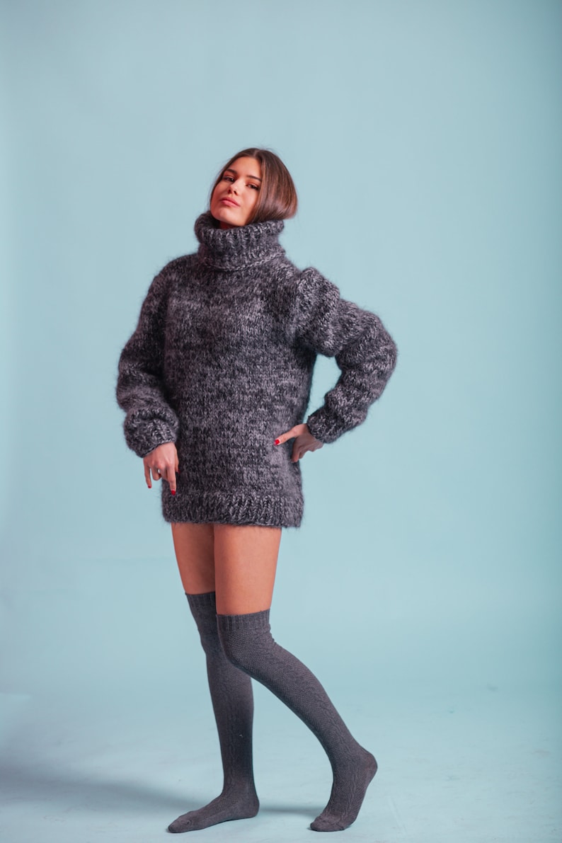 May include: A woman wearing a gray turtleneck sweater and gray knee-high socks. The sweater is a loose fit and has a fuzzy texture.