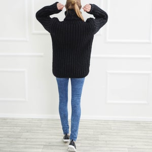 May include: A black, oversized turtleneck sweater with a chunky knit design. The sweater is paired with blue skinny jeans and black sneakers with white soles. The person is facing away from the camera.