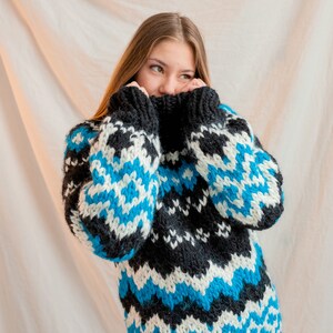 May include: A woman wearing a black, white and blue patterned sweater with a high neck. The sweater has a geometric design.