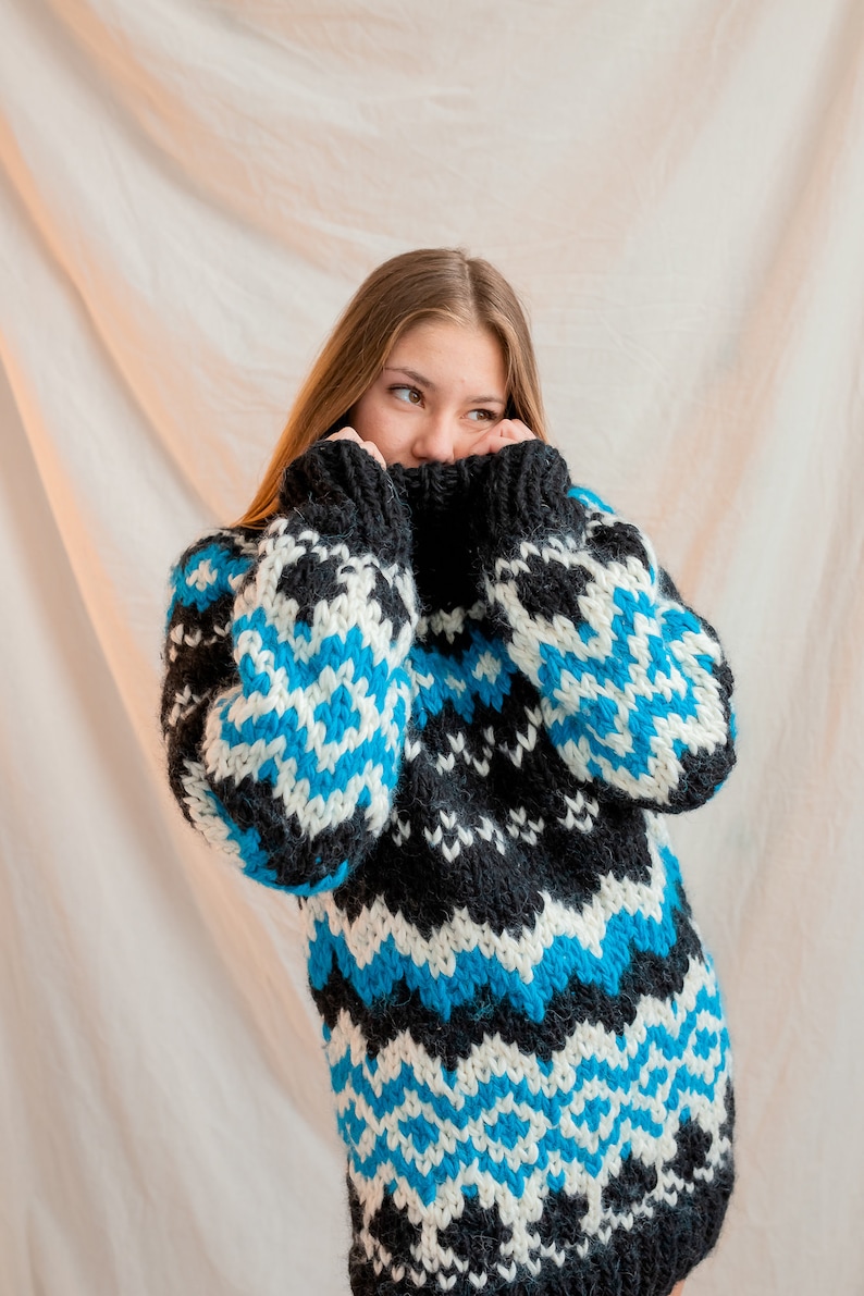 May include: A woman wearing a black, white and blue patterned sweater with a high neck. The sweater has a geometric design.
