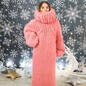 May include: A long, pink knitted sweater with a high turtleneck. The sweater is made of thick yarn and has a loose fit.