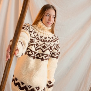 May include: A woman wearing a white and brown knitted sweater with a geometric pattern. The sweater has a turtleneck and long sleeves.
