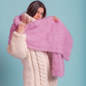 May include: A woman wearing a white cable knit jumper with a pink fluffy scarf draped over her shoulders.