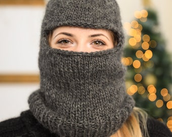 May include: A gray knitted balaclava with a fold-down brim, covering the face of a person with long blonde hair.