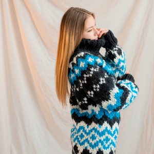 May include: A woman wearing a black, white and blue patterned sweater with a turtleneck. The sweater has a geometric design.