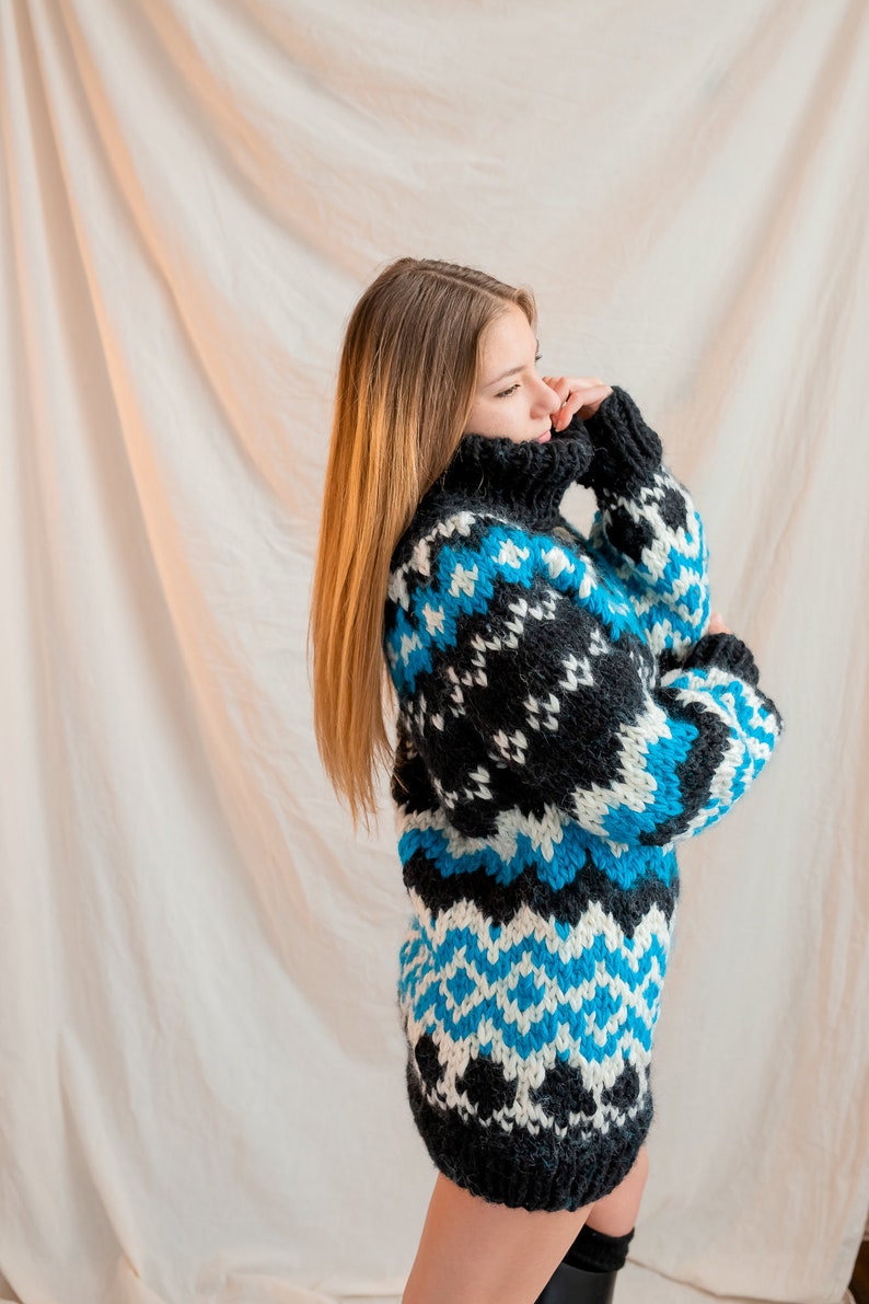 May include: A woman wearing a black, white and blue patterned sweater with a turtleneck. The sweater has a geometric design.