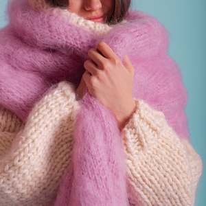 May include: A woman wearing a white and pink knitted jumper with a fluffy pink scarf wrapped around her neck.