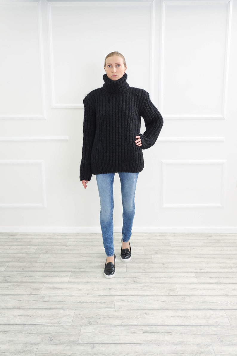 May include: A black, chunky knit turtleneck sweater paired with light blue denim jeans and black loafers. The sweater has a ribbed texture and a high, folded collar. The jeans are fitted, and the loafers have a classic design.