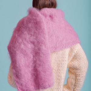 May include: A person wearing a cream knitted sweater with a pink fluffy scarf draped over their shoulders.