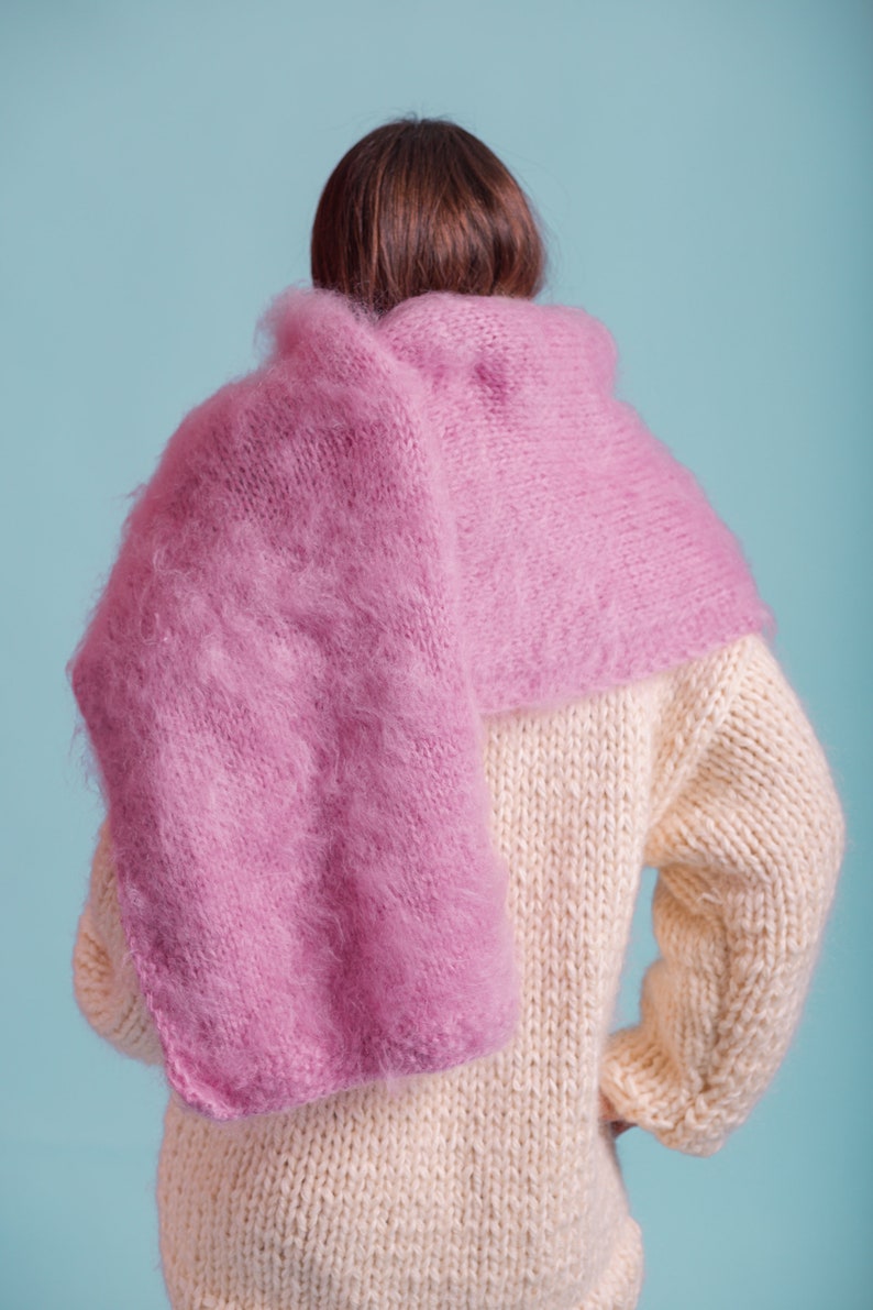 May include: A person wearing a cream knitted sweater with a pink fluffy scarf draped over their shoulders.