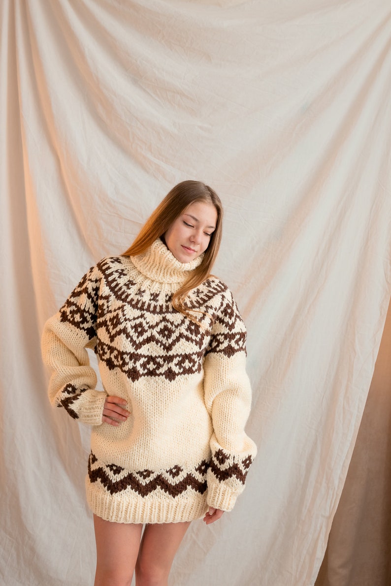 May include: A woman wearing a white and brown patterned sweater with a turtleneck. The sweater has a geometric design.