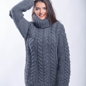 May include: A gray cable knit turtleneck sweater with a loose fit. The sweater is made of a thick, chunky yarn and has a relaxed, comfortable look.
