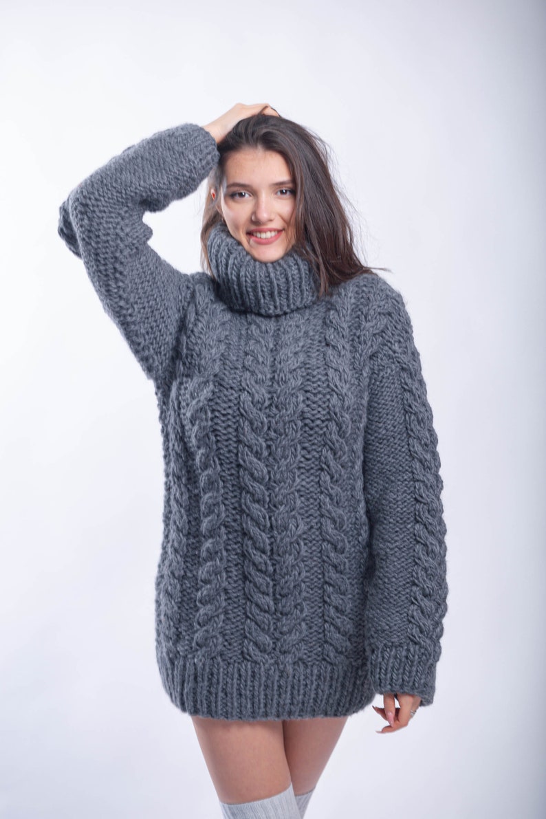 May include: A gray cable knit turtleneck sweater with a loose fit. The sweater is made of a thick, chunky yarn and has a relaxed, comfortable look.