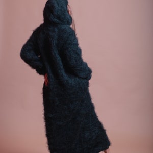 May include: A long, black, fuzzy hooded cardigan with a loose fit. The cardigan is made of a soft, fluffy material and has a relaxed, casual style.