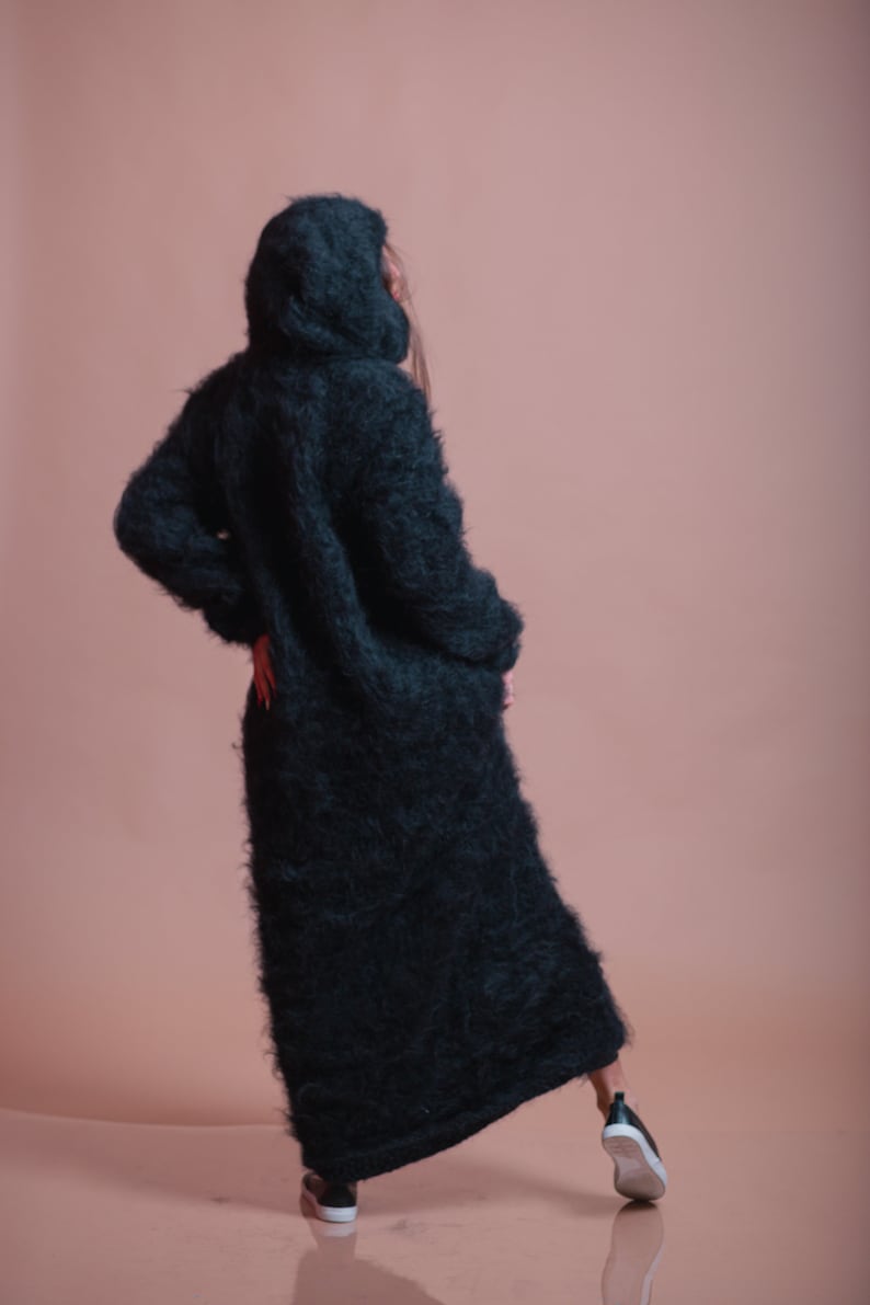 May include: A long, black, fuzzy hooded cardigan with a loose fit. The cardigan is made of a soft, fluffy material and has a relaxed, casual style.