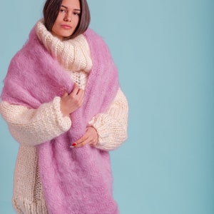 May include: A woman wearing a white and pink knitted jumper with a fluffy texture. The jumper has a turtleneck and long sleeves.