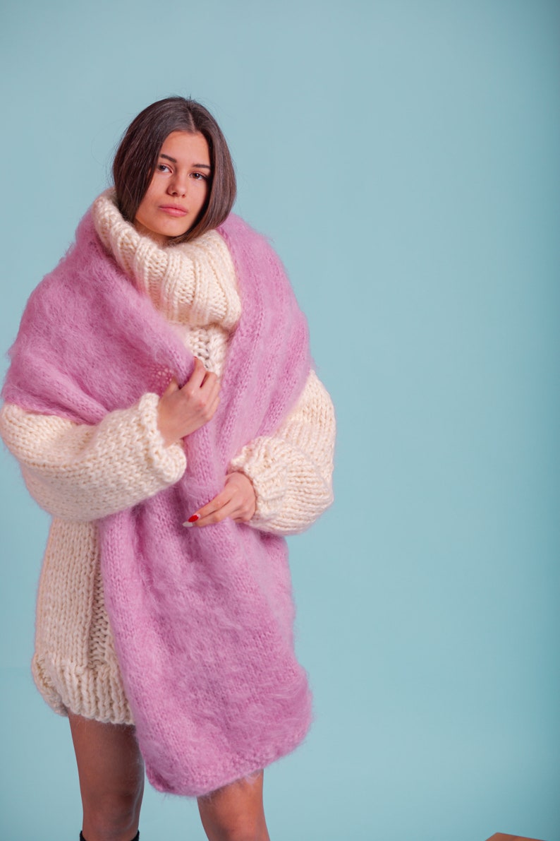 May include: A woman wearing a white and pink knitted jumper with a fluffy texture. The jumper has a turtleneck and long sleeves.