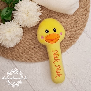 Könnte beinhalten: Gelber Plüsch-Rassel in Form einer Ente mit einem lächelnden Gesicht und dem Text "Naak Naak" auf dem Griff gestickt.