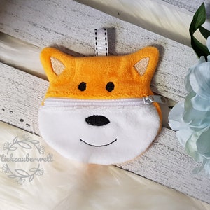 May include: A small orange and white plush fox-shaped zippered pouch with a black embroidered nose and eyes. The pouch has a white zipper and a white loop for hanging.