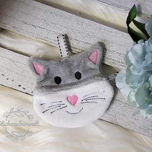 May include: A gray and white plush cat-shaped zippered pouch with pink embroidered details. The pouch has a black ribbon loop for hanging.
