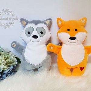 May include: Two plush toys, a gray raccoon and an orange fox, are standing side-by-side on a white fluffy surface. Both toys have white faces with embroidered features and paw prints on their hands.