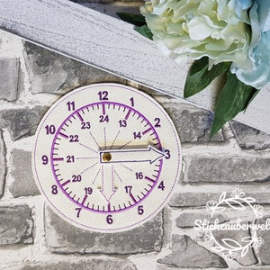 May include: A white circular fabric compass with purple numbers and markings. The compass has a needle pointing to the number 3.
