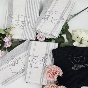 May include: Five kitchen towels with gray and white stripes. Each towel features a different embroidered design of kitchen tools and a heart. One towel is black with a white embroidered design.