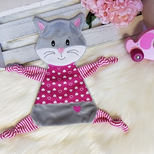 May include: A gray and pink cat-shaped security blanket with a pink heart pattern and pink and white striped arms.