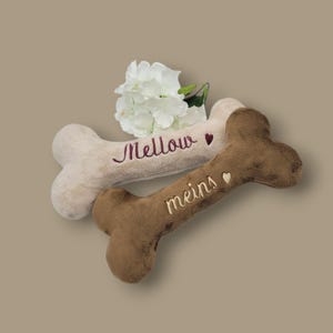 Puede incluir: Dos huesos de peluche para perros, uno beige y otro marrón, con corazones bordados y las palabras "Mellow" y "meins".