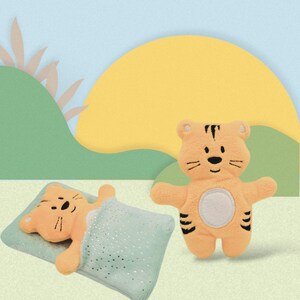 May include: A plush orange tiger toy with black stripes is standing on a light blue background. A second plush tiger toy is lying down on a green and white patterned pillow.