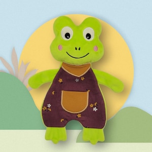 May include: A plush green frog toy with large eyes, rosy cheeks, and a smiling mouth. The frog wears a burgundy corduroy overall with a mustard-colored pocket and floral accents. The background features a yellow circle and a light blue backdrop.
